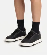 Championes de estilo urbano inspirados en el skate, confeccionados en poliuretano color negro con suela bicolor blanca y negra. Cuentan con cordones negros, perforaciones en la puntera y detalles de recortes en la capellada.