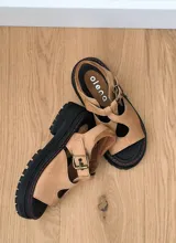 Sandalias de cuero color marrón claro, con suela de goma negra y pespuntes rojos.