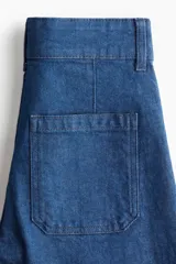 Jean de tiro alto con pierna amplia y corte tobillero. Confeccionado en denim de algodón con leve elasticidad, presenta un pliegue cosido vertical en el frente, cierre con botón y bolsillos traseros de parche.