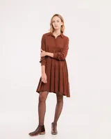 Vestido corto marrón con cuello camisero, abotonado en el frente, mangas largas con elástico en los puños y falda escalonada con volados.