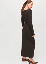 Vestido largo de color marrón, de corte recto, con escote bote y mangas largas. Presenta un diseño ajustado con sutil fruncido a los lados en la zona de la cintura.