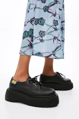 Zapato blucher acordonado de piel color blanco con ojetes metálicos y etiqueta textil personalizada en el lateral. Plataforma de goma logotipada color negro.