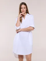 Vestido corto blanco de algodón, marca Dash, con cuello camisero, escote en V y bolsillos laterales. Presenta mangas tres cuartos y calce holgado con ruedo irregular.