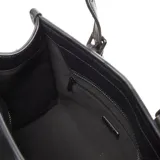 Cartera mediana tipo tote con cuerpo tejido en rafia de color beige y detalles en cuero sintético negro, incluyendo asas de mano, ribetes y correas frontales decorativas con hebillas. Cuenta con una correa larga ajustable y desmontable, y placa metálica con el logo de la marca en el frente.