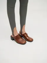 Zuecos de cuero vacuno con acabado en charol, color beige. Presentan un diseño clásico con taco cuadrado de madera de 5 cm y correa trasera ajustable con hebilla metálica.