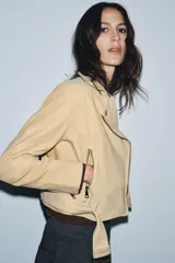 Chaqueta estilo biker de piel de ante 100% color beige, con cuello solapa, manga larga, bolsillos con cremalleras metálicas y bajo ajustable con hebilla. Cierre frontal con cremallera metálica.