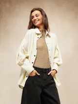 Camisa de pana color crema, con cuello camisero, botones negros en el frente y mangas largas abullonadas con puños.