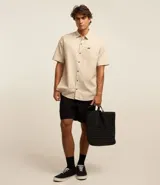 Camisa de corte relajado para hombre, confeccionada en una mezcla de cáñamo y algodón. Presenta cuello inglés, manga corta, cierre frontal con botones y un bolsillo en el pecho con una pequeña etiqueta aplicada.