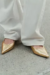 Zapatos tipo kitten heel destalonados, de color dorado con acabado metalizado texturizado, tacón bajo ancho y punta fina.