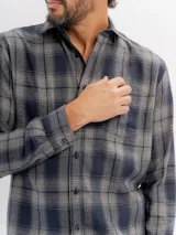 Camisa de franela a cuadros en tonos azul y negro, con cuello clásico, cierre frontal de botones y bolsillo en el pecho.