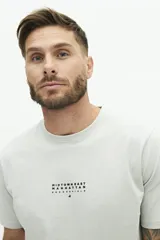 Remera de manga corta color beige con estampado gráfico en la espalda que representa el edificio Chrysler de Nueva York y texto descriptivo.