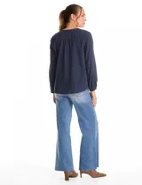 Blusa de algodón azul marino con bordado floral al tono. Presenta escote en V con terminación festoneada y mangas largas ligeramente abullonadas con puños abotonados. Su diseño es de silueta fluida y relajada.