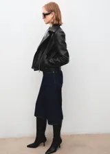 Chaqueta estilo biker de cuero sintético negro, con cierre frontal cruzado, solapas con muesca y broches metálicos.