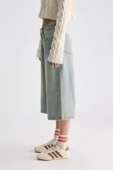 Jean culotte estilo bermuda de tiro bajo, color celeste con efecto desgastado, perneras amplias y corte recto por debajo de las rodillas.