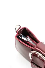 Cartera tipo bandolera de charol rojo, de diseño estructurado, con una hebilla metálica grande decorativa en el frente y correa larga ajustable y desmontable.