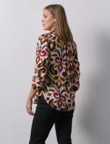 Blusa de gasa estampada con diseño geométrico multicolor, cuello a la base con escote en V y abertura frontal con botones. Presenta detalle de plisado en la parte delantera y mangas largas con sistema de ajuste mediante presilla y botón.