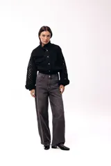 Campera de jean negra con mangas largas tejidas en crochet con diseño calado y detalles florales en relieve. Presenta cuello camisero, cierre frontal y bolsillos en el pecho.