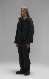 Campera técnica liviana de microfibra negra con acabado mate, capucha ajustable, cierre frontal oculto bajo solapa, bolsillos frontales con solapa y cordón ajustable en la cintura.