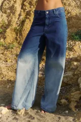 Jean de tiro medio con corte oversize y botamanga ancha. Presenta un diseño de lavado degradado que va de un azul intenso en la cintura a un tono claro en la parte inferior, con efecto gastado. Incluye avíos metálicos y badana de PU.