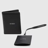 Set de viaje compuesto por un porta pasaporte y un identificador de maleta con correa, ambos en cuero sintético negro con textura granulada y logo de la marca grabado.