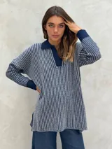 Sweater de punto azul y blanco a rayas verticales, con cuello polo y escote en V. Tiene mangas largas y puños acanalados.
