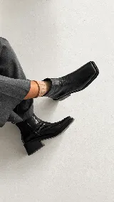 Bota corta de cuero negro con acabado ligeramente envejecido, diseño de punta cuadrada y tacón geométrico. Cuenta con cierre lateral para un calce práctico.