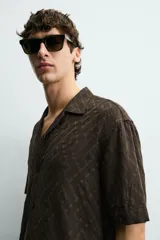 Camisa de corte relajado con cuello bowling y manga corta. Confeccionada en tejido fluido con textura jacquard de patrón geométrico y cierre frontal de botones.