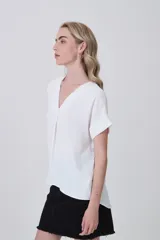 Blusa de poliéster color blanco con cuello en V, mangas cortas con dobladillo y corte holgado.