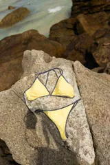 Conjunto de bikini color amarillo pastel con bordes en contraste de rayas azul marino y blanco. El corpiño es de estilo triangular con tiras finas y la bombacha es de corte clásico con tiras laterales ajustables.