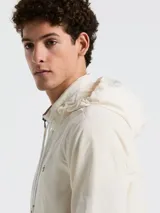 Campera rompevientos color crema con cierre frontal, cuello alto, capucha oculta, puños elásticos y bolsillos laterales con cierre.