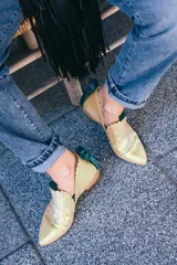 Botín de piel tornasolada con acabado brillante en tono amarillo lima y reflejos verdes. Presenta un diseño de dos piezas con bordes troquelados, aberturas laterales, ajuste con elásticos y un borlón decorativo de ante verde en la parte trasera. Incluye cuña interna y suela de cuero.