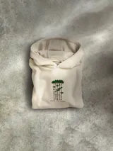 Buzo con capucha color beige, confeccionado en mezcla de algodón. Presenta un diseño bordado y flocado en el centro del pecho inspirado en Bright Tree Village de los Ewoks, con detalles adicionales que incluyen insignias rebeldes, mensajes en Aurebesh y coordenadas de Endor. Cuenta con bolsillo tipo canguro, capucha forrada con costuras Trapunto y puños y dobladillo acanalados.