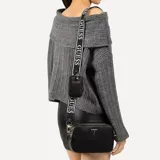 Cartera tipo bandolera Guess modelo Latona II, color negro con textura granulada. Presenta cierre superior, logo triangular metálico en el frente y correa ancha ajustable con el nombre de la marca. Incluye un pequeño monedero rectangular desmontable sujeto a la correa.