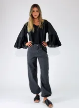 Pantalon de denim azul oscuro con diseño de rayas diplomáticas blancas, de corte holgado y silueta abombada en los tobillos.