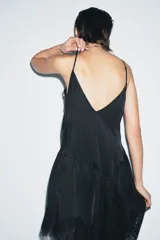 Top negro de tirantes finos con escote pico. Presenta bordados ornamentales en el frente y detalles de puntilla en el escote y el bajo asimétrico.