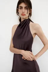Vestido largo de satén negro con cuello halter y escote fluido. Presenta cierre con cremallera oculta en la espalda y lazada en el cuello.