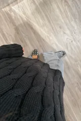 Sweater de punto negro con diseño de trenzas verticales, cuello redondo y corte holgado con aberturas laterales en el ruedo.