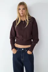 Sweater de punto color marrón oscuro, con cuello polo y cierre frontal parcial. Presenta mangas largas con puños anchos acanalados y un acabado acanalado en el bajo.