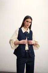 Chaleco azul de denim con cuello en V y cierre frontal con botones metálicos. Posee bolsillos delanteros y corte clásico.