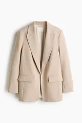 Blazer de sarga color beige, con solapas de pico, frente abierto y bolsillos delanteros ribeteados con solapa.