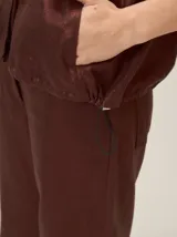 Chaqueta de lino y rayón color tostado, de corte holgado, mangas cortas amplias, cuello mao y cierre frontal oculto con cremallera. Presenta pespuntes a contratono en las costuras y cordón ajustable en el bajo.