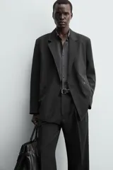 Blazer negra de corte relajado confeccionada en tejido con mezcla de lyocell. Tiene cuello con solapas de muesca, manga larga con puños abotonados, bolsillos de doble vivo en la cadera, bolsillo interior y cierre frontal cruzado con botones.