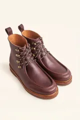 Bota de cuero vacuno color bordó con acabado charol, diseño de caña media con cordones y ganchos metálicos. Presenta costuras visibles en la puntera y suela de goma tipo crepe.