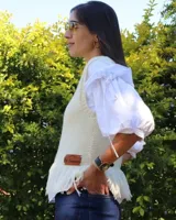 Chaleco de punto tejido a mano con lana merino, color blanco, con cuello redondo, detalles de flecos en el ruedo y aplique de etiqueta de cuero con la marca.