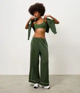 Pantalón deportivo ancho de color verde oscuro, de talle alto con cintura elástica y detalles de vivos en color blanco en los laterales y la botamanga.