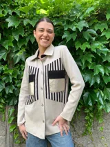 Camisa color beige con detalles de cuero negro en los bolsillos y en la parte superior del frente, de lana merino, con cuello clásico y cierre con botones.