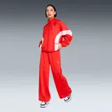Campera Puma modelo Wardrobe Essentials, color rojo con bandas blancas en las mangas y el torso, cuello semi-alto y cierre frontal. Incorpora tecnología windCELL para protección contra el viento y cuenta con el logo de la marca bordado en el pecho.