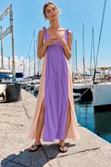 Vestido largo de viscosa con diseño bicolor que combina lila en el centro y beige en los laterales, con tirantes ajustables mediante lazos y aberturas laterales en la falda.