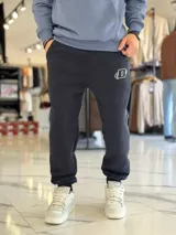 Pantalón jogger negro de corte oversize con felpa, bolsillos laterales y puños elásticos en los tobillos. Presenta un pequeño logo estampado en color blanco en la pierna izquierda.