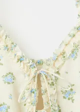 Top de tirantes finos en color beige con estampado floral pequeño y detalles de volados en los bordes. Cuenta con cierre frontal de cordones tipo lazo.
